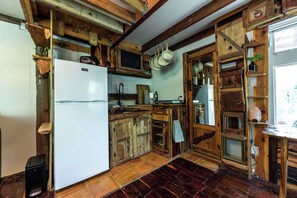 A rustic kitchen with wooden cabinets, a white refrigerator, and a tiled floor. - Tranquil Cedar Cabin, Nature Retreat (Paige)