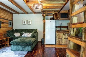 Un espace de vie compact avec un canapé vert, des murs en bois, un réfrigérateur blanc et un coin cuisine doté de meubles en bois.