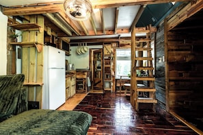 A rustic interior with a wooden floor, a bed, a kitchen area with a refrigerator, and a dining table. - Tranquil Cedar Cabin, Nature Retreat (Paige)