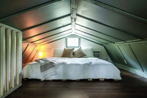 Un dormitorio con techo inclinado, cama con almohadas, una ventana y un calentador de pared.
