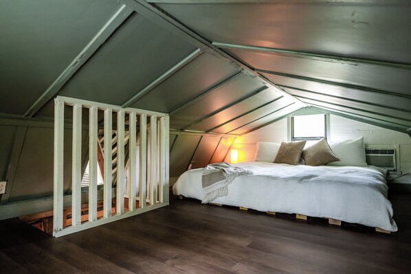 Ein Schlafzimmer mit Schräge, einem Bett mit Kissen, einem Fenster und Holzboden.