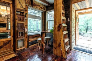 A rustic cabin interior with wooden walls, a wooden bench, and a window overlooking a forest. - Romantic Getaway, King Bed, Nature! (Paige)