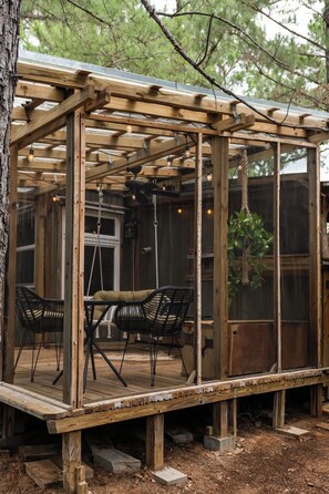 A wooden pergola structure with a glass enclosure, two black wicker chairs, and a hanging plant. - Tranquil Cedar Cabin, Nature Retreat (Paige)