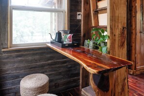 Una mesa de madera con una cafetera y un paquete de café, una ventana y una planta.