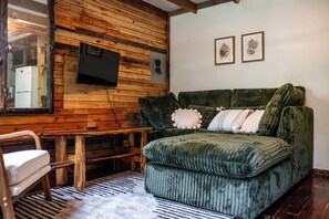 A room with a wooden wall, a green sofa, a small table, and a chair. - Tranquil Cedar Cabin, Nature Retreat (Paige)