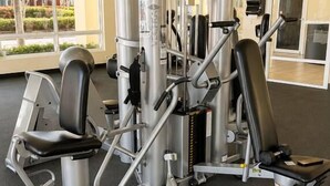 Un gimnasio con diversas máquinas de ejercicio, amplias ventanas y un televisor de pantalla plana montado en la pared.