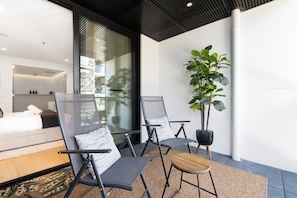 A modern hotel room with a bed, two chairs, a small table, and a potted plant. - High-End 1BR with Enclosed Balcony Near ANU (Braddon)