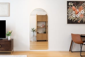 A room with a wooden cabinet, a television, a mirror, a chair, and a painting. - High-End 1BR with Enclosed Balcony Near ANU (Braddon)