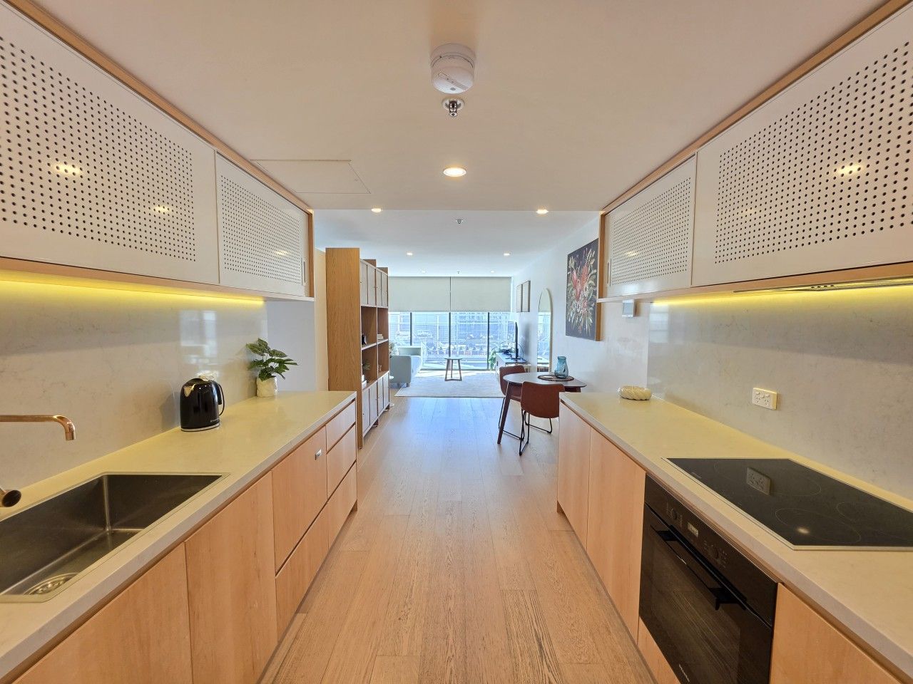 A modern kitchen with a central island, wooden cabinets, and a view to the outside.