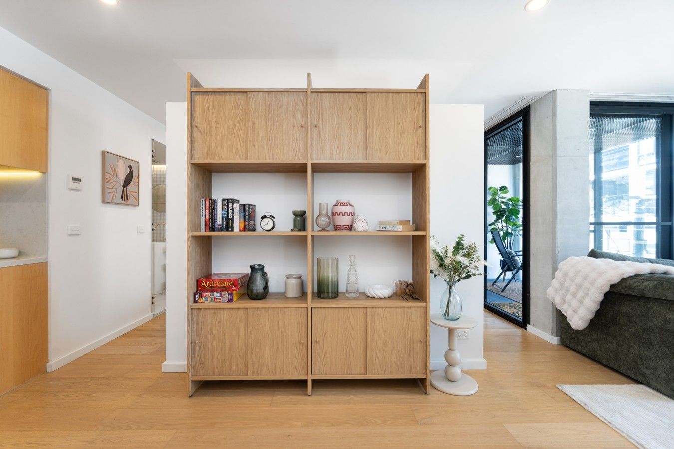 Una sala de estar moderna con una estantería de madera, una pequeña mesa redonda con un florero y un sofá gris.