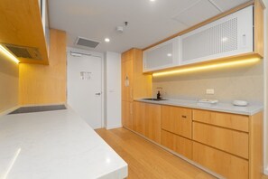 A modern kitchen with wooden cabinets, a white countertop, and a built-in microwave. - High-End 1BR with Enclosed Balcony Near ANU (Braddon)