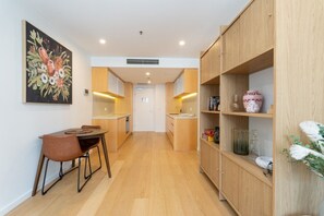 A modern kitchen with wooden cabinets, a dining area with a table and chairs, and a hallway leading to a door. - High-End 1BR with Enclosed Balcony Near ANU (Braddon)