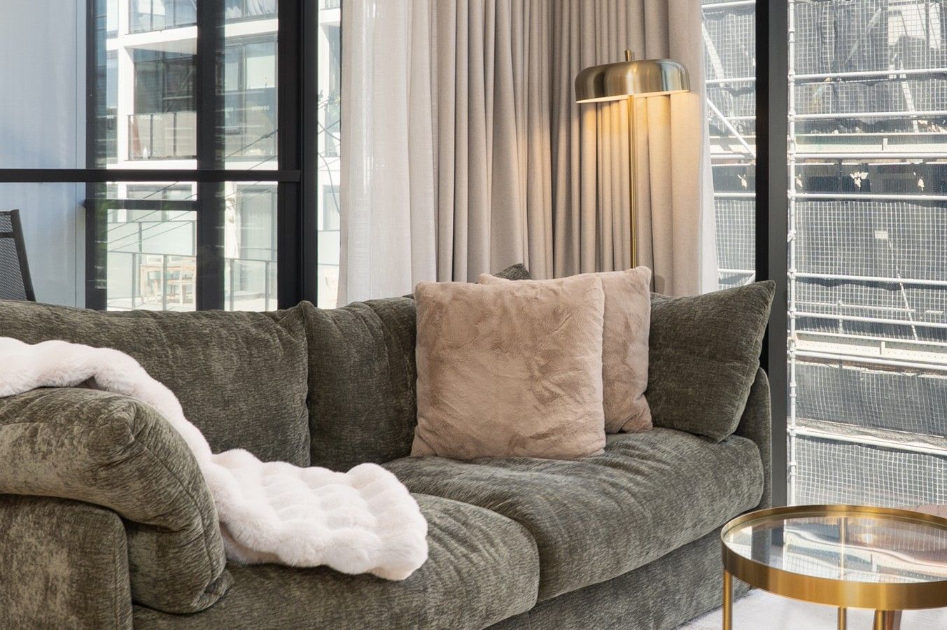 Una sala de estar moderna con un sofá gris, una manta blanca y una mesa de centro redonda de vidrio.