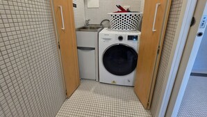 Een kleine wasruimte met een wasmachine, een klein wastafeltje en een droogrek.