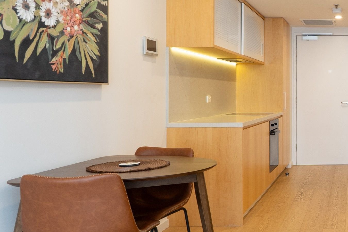 Una cocina moderna con armarios de madera, horno empotrado y comedor con mesa y sillas.