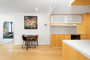 A modern kitchen with wooden cabinets, a white countertop, and a dining area with a table and chairs. - High-End 1BR with Enclosed Balcony Near ANU (Braddon)