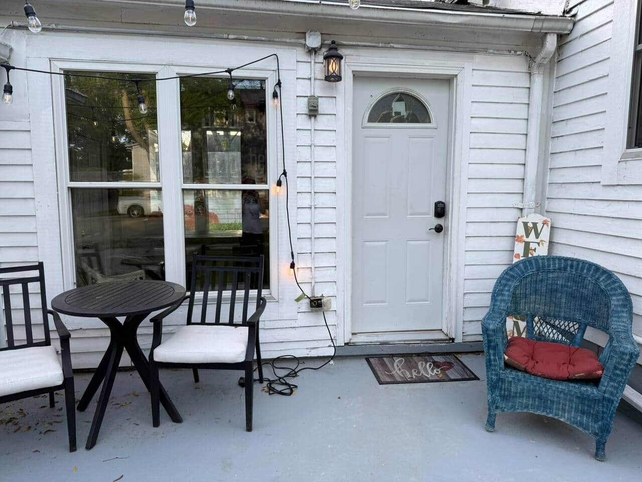 A porch with a table and chairs, a door, and a decorative sign.