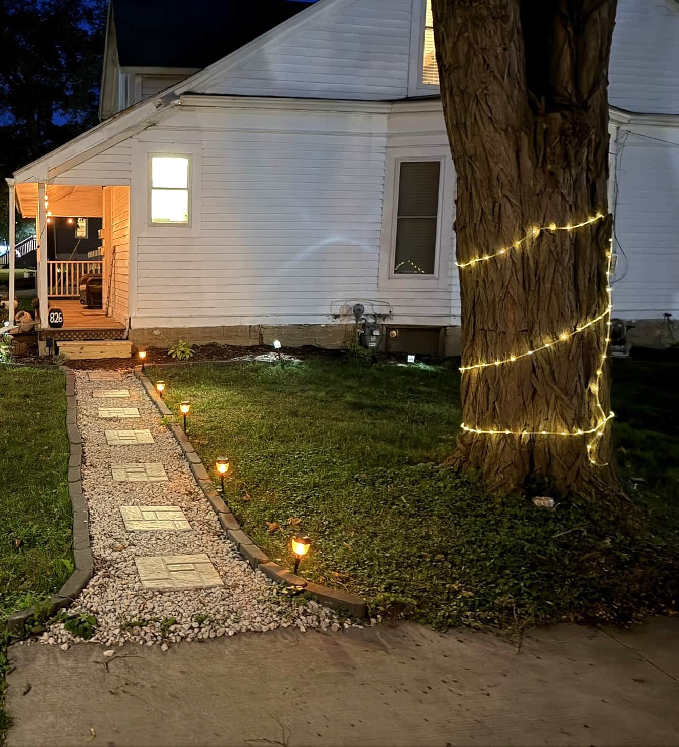 Une maison avec un chemin pavé menant à la porte d’entrée, un arbre décoré de guirlandes lumineuses et une boîte aux lettres portant le numéro 826.