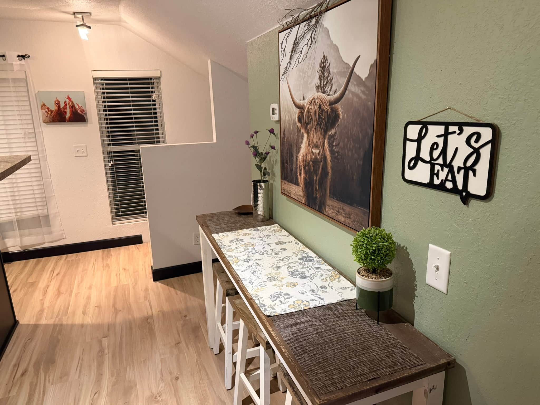Una cocina moderna con una mesa de madera, una planta en maceta y un letrero en la pared.