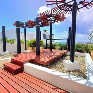 A modern outdoor area with a wooden deck, metal poles, and a unique red and black sculpture. - Studio Blue Playa del Carmen (Playa del Carmen)