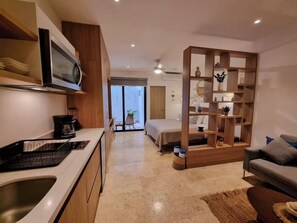 A modern kitchen with a microwave, coffee maker, and a sink. There is a bed with a wooden headboard and a small table with a basket. A sofa is visible in the foreground. - Studio Blue Playa del Carmen (Playa del Carmen)