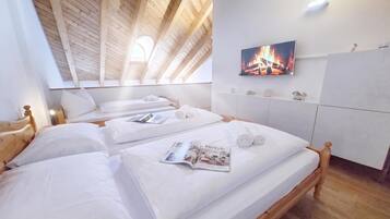 A room with two beds, a television mounted on the wall, and a wooden ceiling.