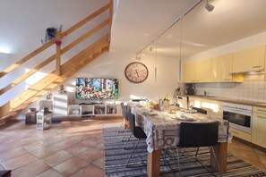 Een eetgedeelte met een tafel voor twee, een keuken met gele kastjes en een trap met houten leuningen.