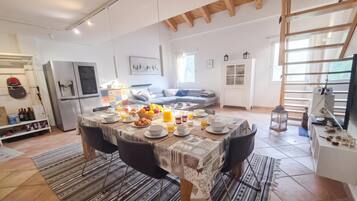 A spacious living area with a dining table set for breakfast, a sofa, and a kitchen area with a refrigerator.