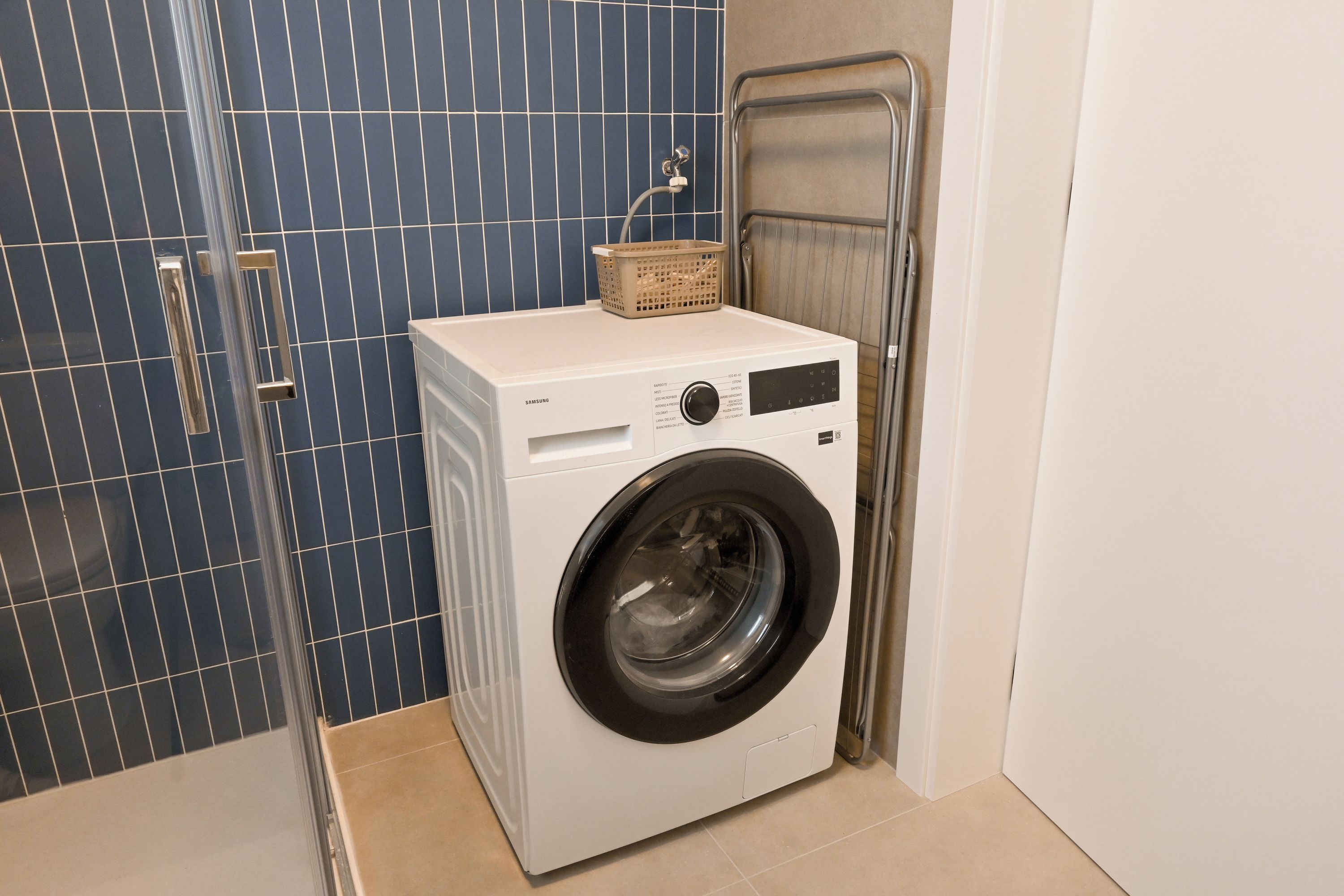 Une machine à laver à chargement frontal dans une salle de bain avec un mur recouvert de carreaux bleus et un porte-serviettes en métal.