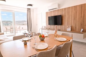 Ein moderner Essbereich mit einem großen Tisch für vier Personen, einem an einer Holzwand montierten Flachbildfernseher und einem Balkon mit Sitzgelegenheit im Freien.