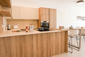 Eine moderne Küche mit Holzausstattung, einem Einbauofen und einer Arbeitsfläche mit Wasserkocher, Schneidebrett und Gemüse.