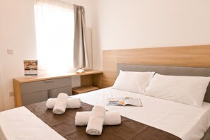 A hotel room with a bed, a bedside table with a book, and a window with curtains. - Penthouse, Jacuzzi & Sea-View in Gozo 7A, Marsalforn Iz-Zebbug Gozo, Malta (Marsalforn Iz-Zebbug Gozo)