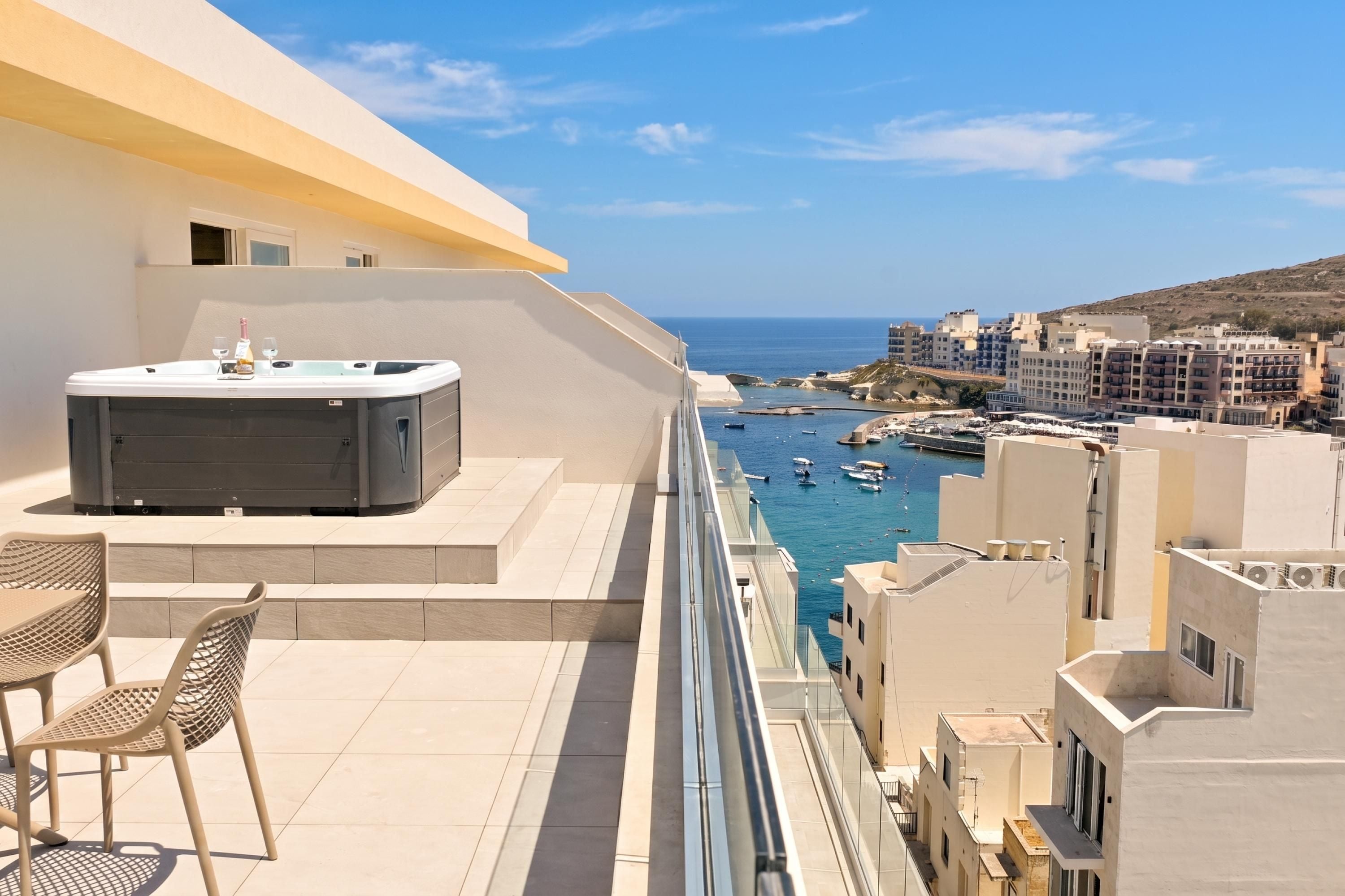 Ein Balkon mit Whirlpool, Stühlen und Blick auf das Meer und die Gebäude.