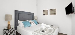 A hotel room with a bed, two bedside tables, a flat-screen TV, and two wall-mounted picture frames. - Devlin 103 - Stylish Geelong Apartment (Greater Geelong)