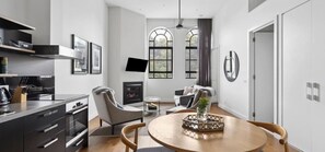 A modern living room with a fireplace, a dining table with chairs, and a kitchen area with cabinets and a stove. - Devlin 103 - Stylish Geelong Apartment (Greater Geelong)