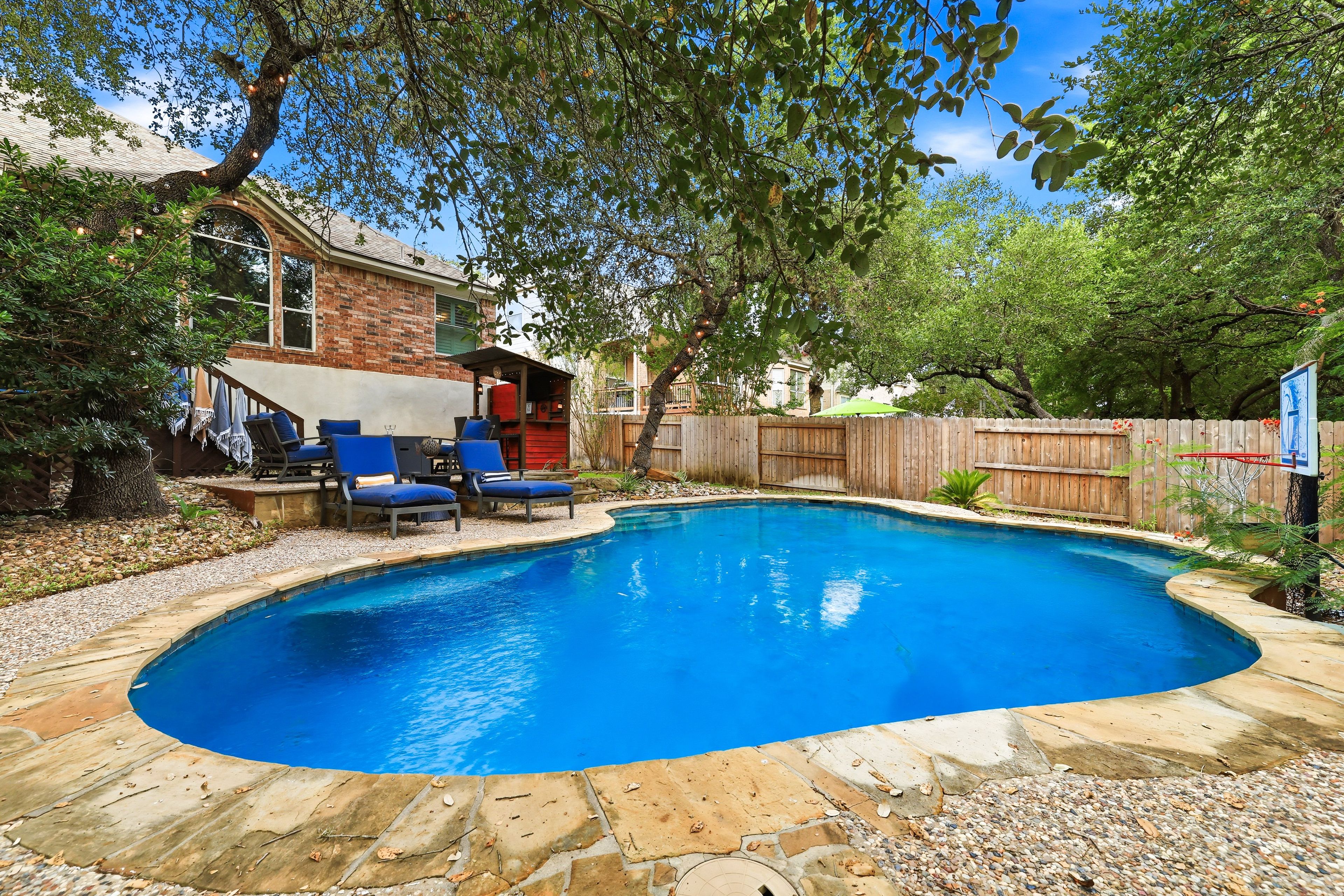 A backyard with a swimming pool, a covered seating area, and a wooden fence.