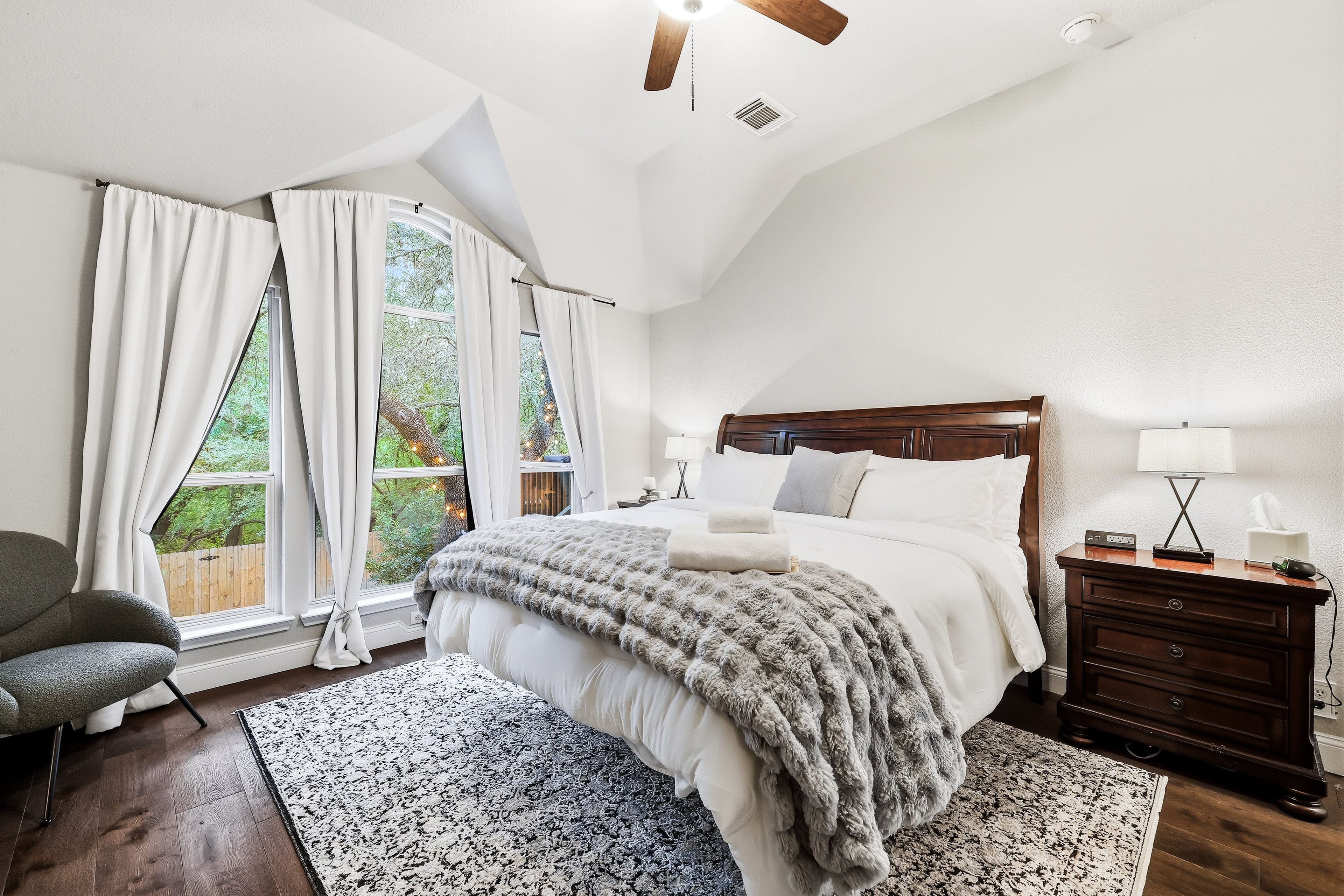 A bedroom with a large bed, a wooden headboard, a nightstand, a lamp, and a chair.