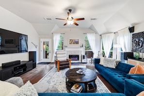 A spacious living room with a fireplace, a blue sofa, a coffee table, and a ceiling fan. - Walcoff - A Birdy Vacation Rental (Schertz)