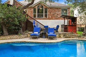 A backyard with a swimming pool, a brick house, and outdoor seating.