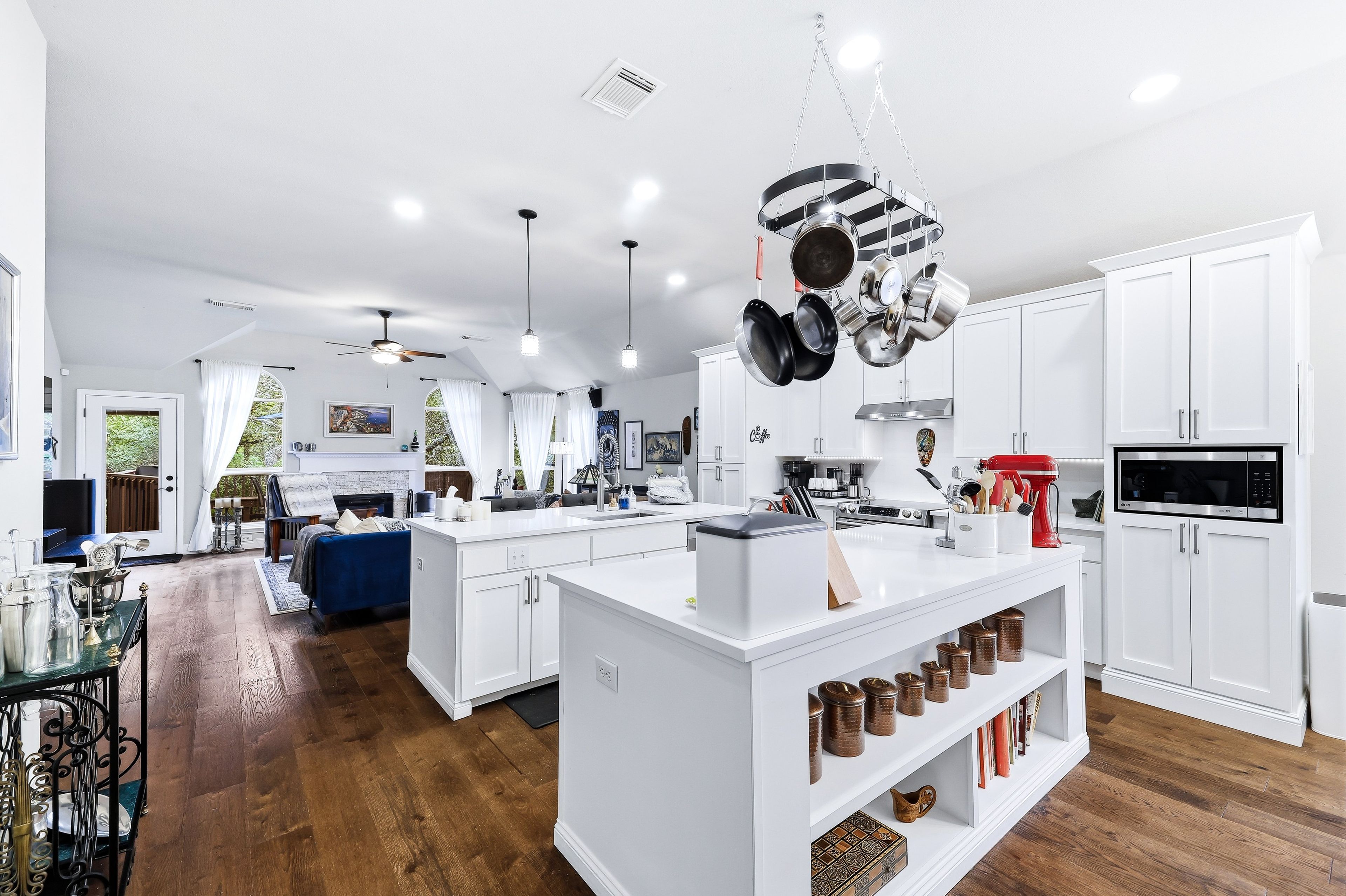 A modern kitchen with white cabinetry, a central island, hanging pots, and a red stand mixer.