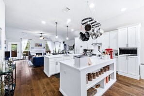 A modern kitchen with white cabinetry, a central island, hanging pots, and a red stand mixer.