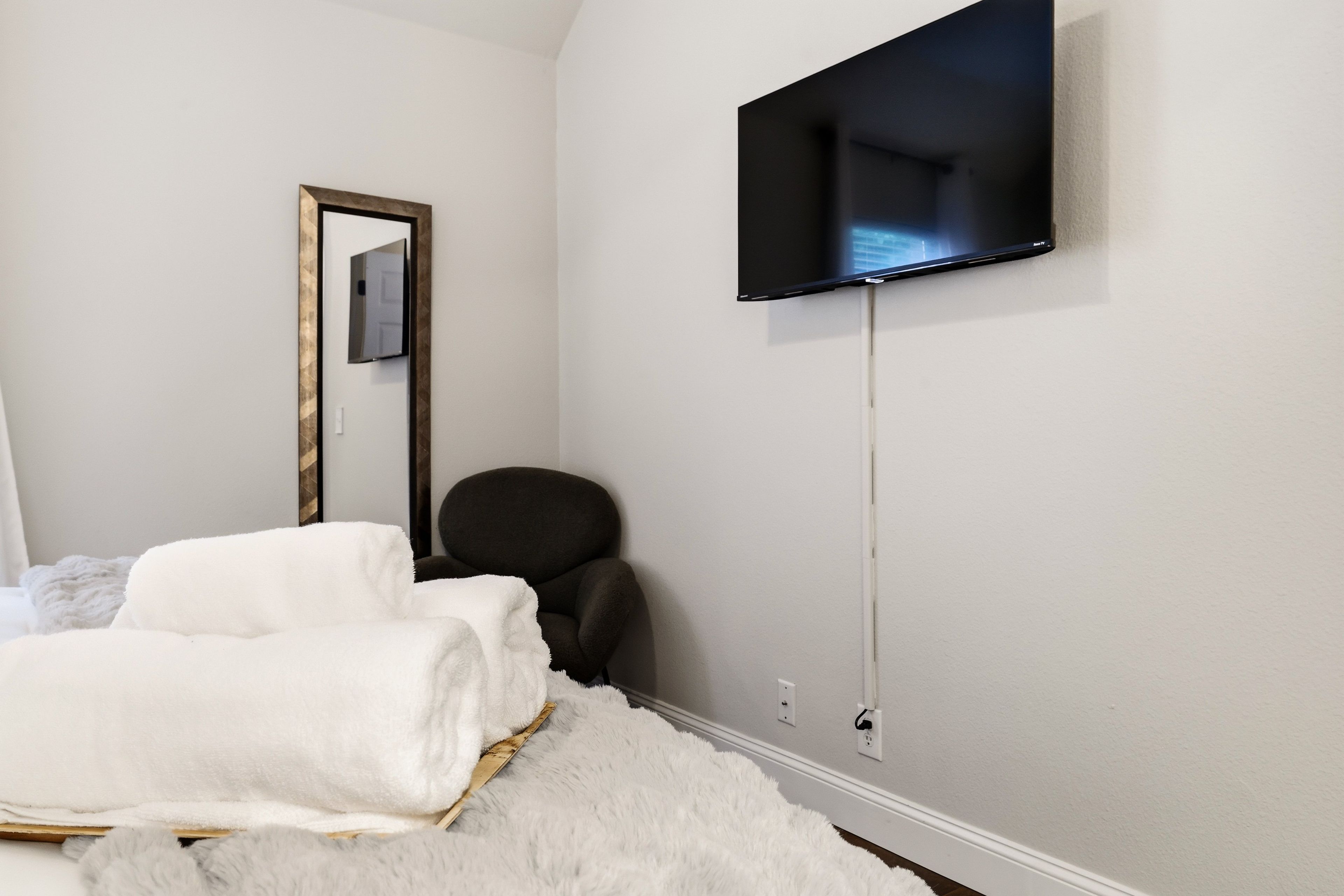 Une chambre à coucher comprenant un lit, une chaise, un téléviseur fixé au mur et un miroir.