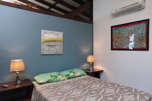 Ein Schlafzimmer mit einem Bett, zwei Nachttischlampen, einer Wandklimaanlage und zwei Kunstwerken.