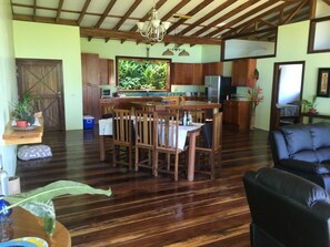 Eine geräumige Küche mit Holzausstattung, ein Essbereich mit Tisch und Stühlen sowie ein schwarzes Ledersofa.