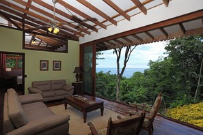 Ein Wohnzimmer mit großem Fenster, Deckenventilator und Blick ins Freie.