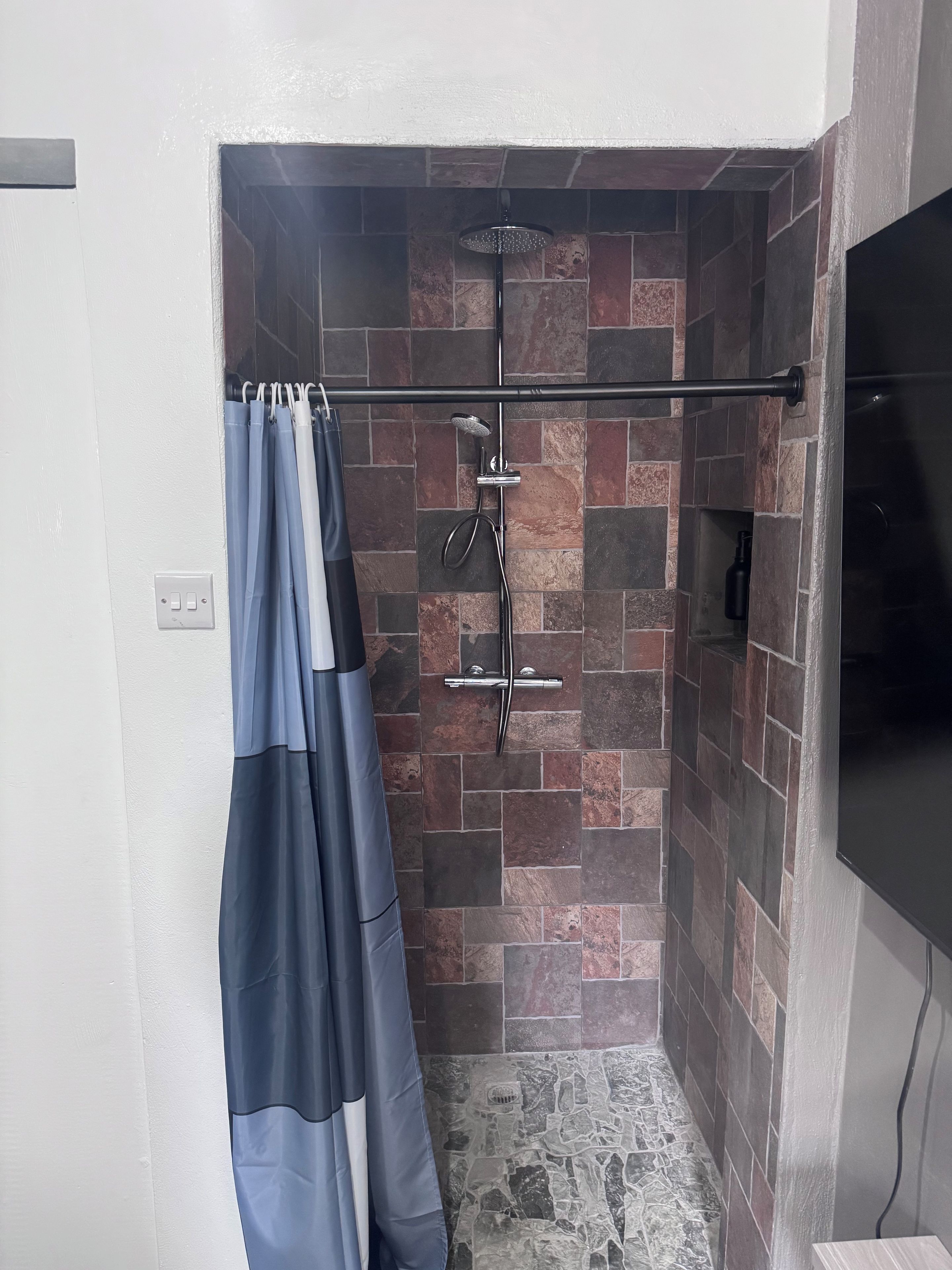 Un espace douche équipé d’une pomme de douche à pluie et d’un pommeau de douche à main, d’un rideau et d’un mur au motif de pierres.