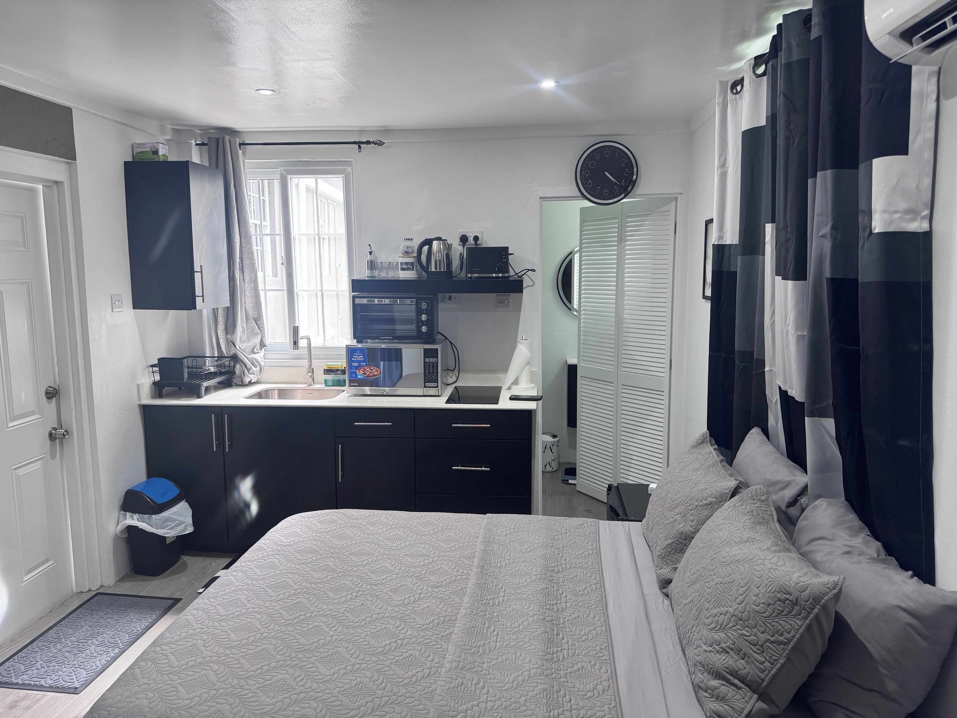 Une chambre à coucher avec un lit, une table de chevet, une fenêtre avec des rideaux, une armoire et une horloge au mur.