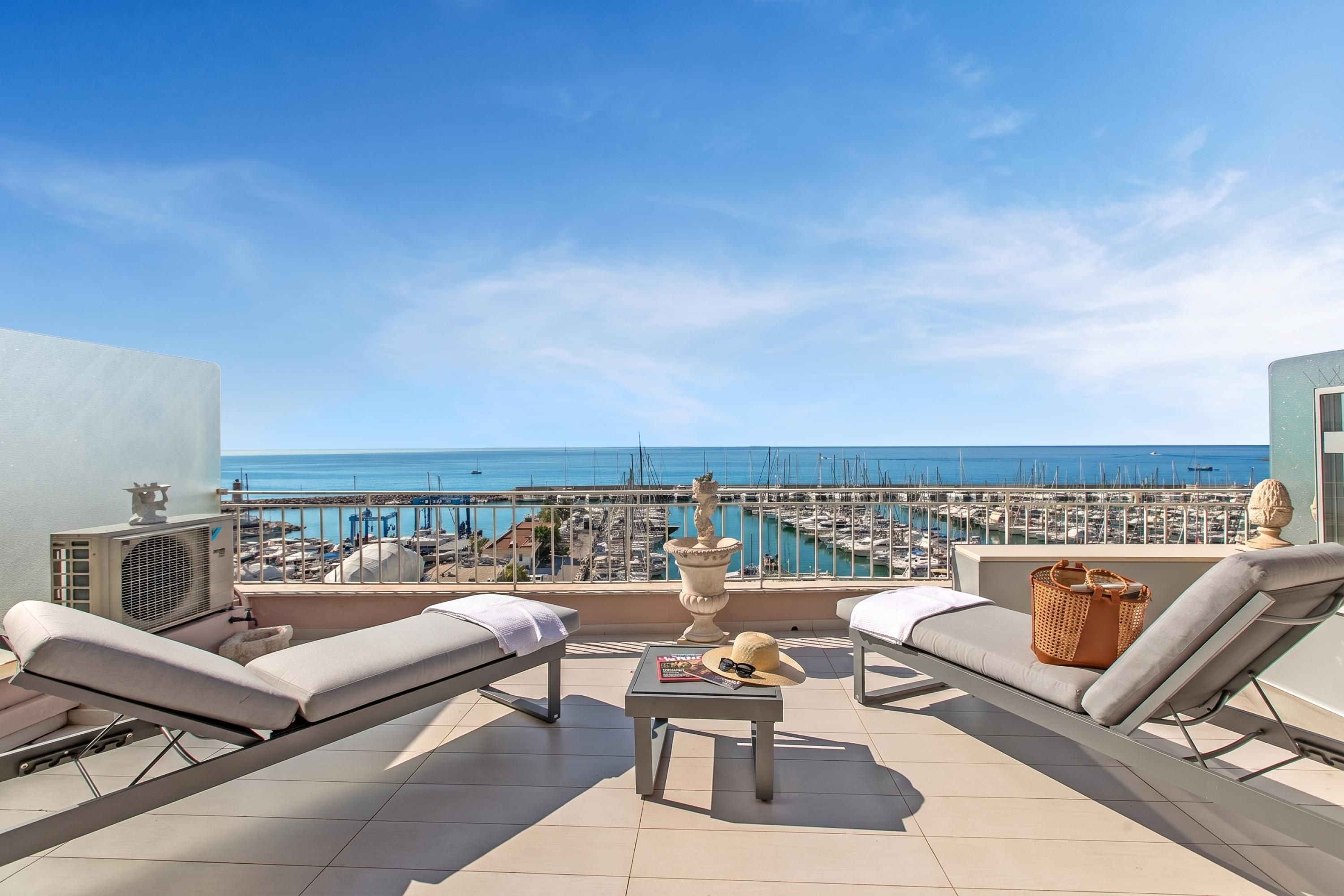 Une terrasse sur le toit, équipée de deux chaises longues et d’une petite table, offrant une vue sur une marina et ses bateaux.