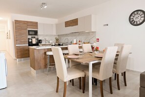 A modern kitchen with a central island, white cabinets, and a dining area with six chairs and a table set for four. - Comfort & Modern Sea-View 3 bdr Apart, Saint Paul's Bay, Malta (Saint Paul's Bay)