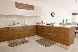 A modern kitchen with wooden cabinets, a marble backsplash, a stainless steel sink, and a dining area with a table and chairs. - Comfort & Modern Sea-View 3 bdr Apart, Saint Paul's Bay, Malta (Saint Paul's Bay)